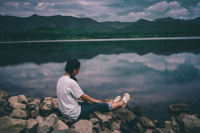 Woman sitting on rock at lakeshore against mountains