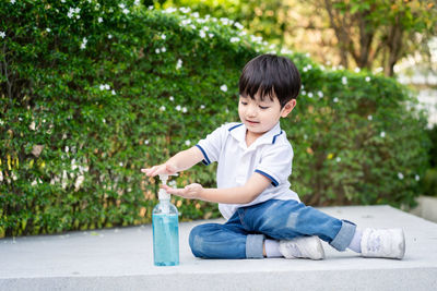 Cute boy applying sanitizer against plants