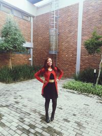 Full length portrait of young woman standing against building