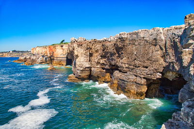 Rock formations by sea against clear blue sky