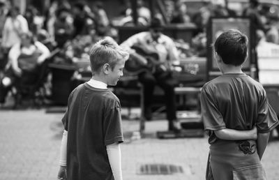 Rear view of boys looking at street musician performing in city