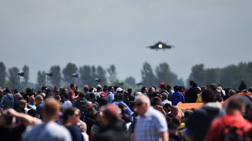 Crowd watching military airplane flying in sky