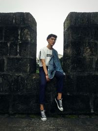 Full length portrait of young woman standing against brick wall