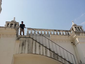 Low angle view of man standing by railing on building against sky