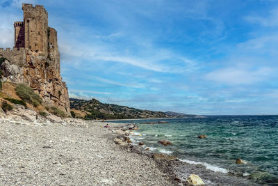 The beach of roseto capo spulico with turquoise water and a castle above it