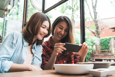 Young woman using phone while sitting on table