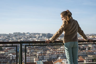 Rear view of woman standing by railing against sky in city
