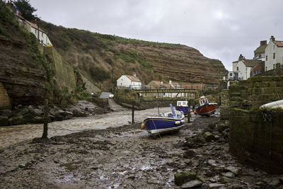 Boats moored on land by buildings against sky