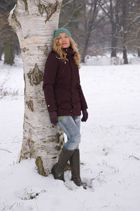 Portrait of blond woman standing against tree in park