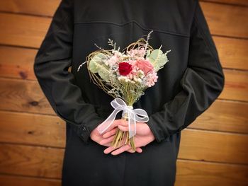 Midsection of man holding flower bouquet against wooden wall