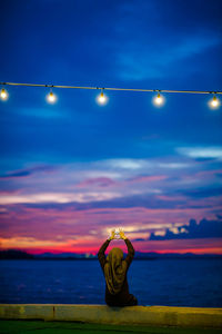 Rear view of woman making heart shape while sitting on retaining wall by sea