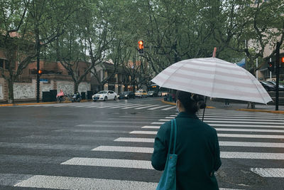 Rear view of woman holding umbrella while standing on road