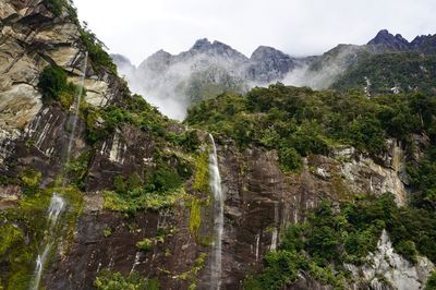 Scenic view of waterfall against mountains and clouds