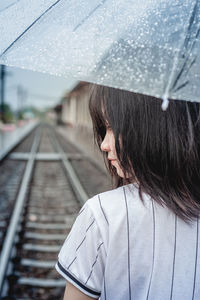 Rear view of girl with umbrella on railroad track