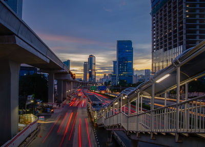 Light trails on road amidst buildings against sky during sunset