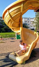 Rear view of girl sitting on slide at playground