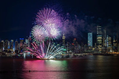 Firework display over illuminated city against sky at night