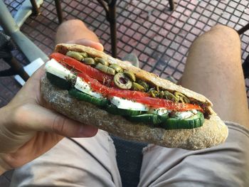 Cropped image of man having sandwich while sitting at outdoor restaurant