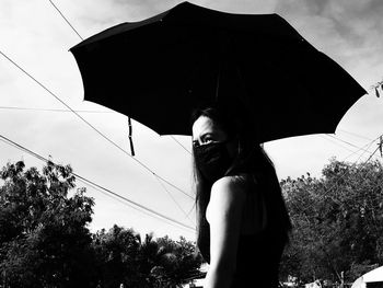 Low angle view of woman standing with umbrella against sky