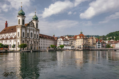 Buildings at waterfront against cloudy sky