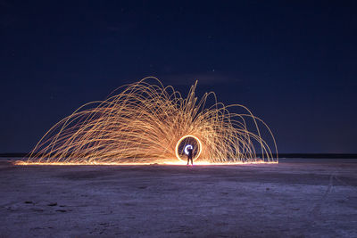 Man with illuminated wire wool on field against sky