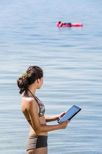 Woman using phone while standing on sea