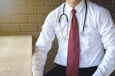 Midsection of doctor sitting against wall