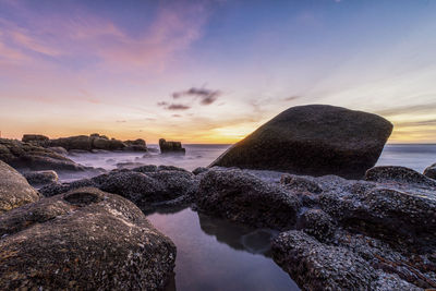 Rocks on beach against sky during sunset