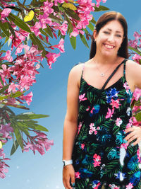 Portrait of smiling young woman standing against pink flowering plants