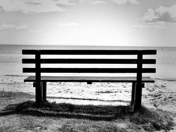 Bench on beach against sky