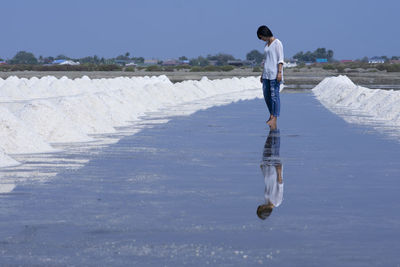 Woman standing on salt flat against clear sky