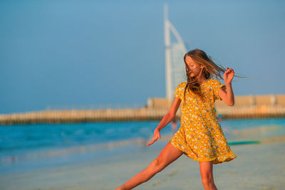 Woman with arms raised on beach against blue sky