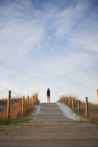 Rear view of woman standing on footpath against sky