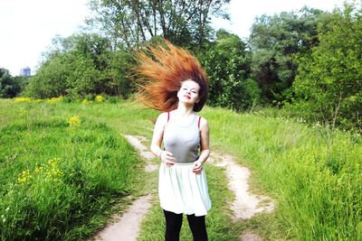 Smiling beautiful woman tossing hair while standing on grassy field