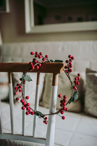 Simple wreath made with decorative red berries placed on chair in cozy room during christmas preparation