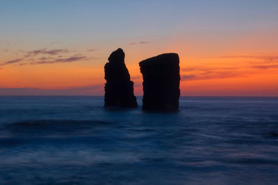 Silhouette rock on sea against romantic sky at sunset