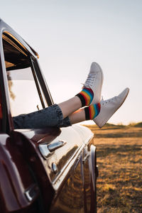 Side view of crop female chilling in vintage car with legs sticking out of window in evening in nature