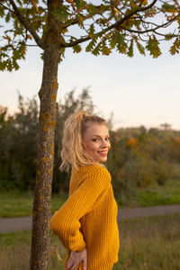 Portrait of smiling young woman standing by tree