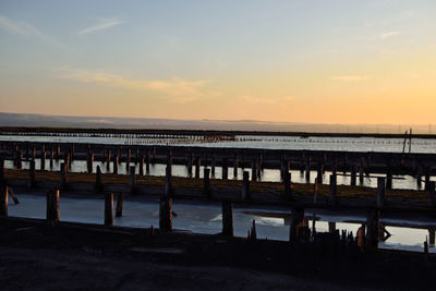 Pier on beach against sky during sunset