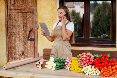 A young female florist with a tablet in her hands is talking on the phone and making an order 