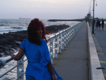 Rear view of woman on railing against sea during sunset