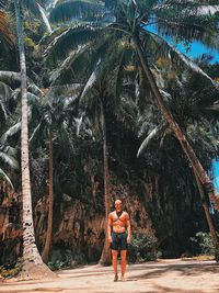 Full length of shirtless man standing by palm tree