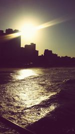 Silhouette city by river against sky during sunset