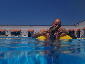Father and son swimming in pool against clear blue sky