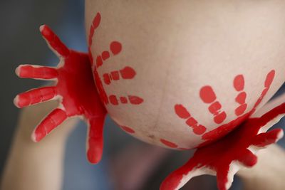 Close-up of cropped hands on red painted pregnant woman belly