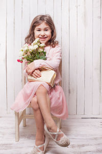 Portrait of happy girl holding pink while sitting against wall