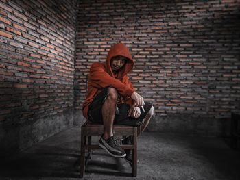 Man sitting on chair against brick wall