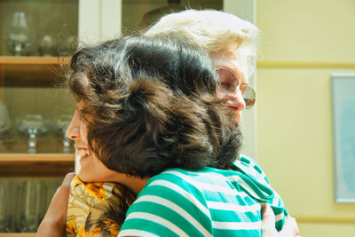 Side view of smiling woman embracing grandmother at home