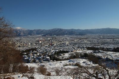 Human settlement by mountains against clear blue sky during winter