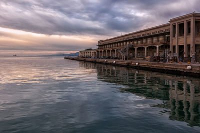 Built structures by sea against cloudy sky